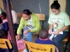 Ashley Walker and other volunteers help tie new shoes on the feet of formerly barefoot children.